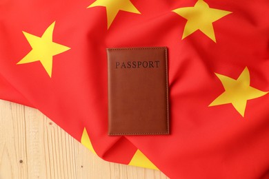 Photo of Passport in brown cover and flag of China on wooden table, top view