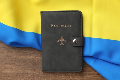 Photo of Passport in black cover and flag of Ukraine on wooden table, top view