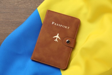 Photo of Passport in brown cover and flag of Ukraine on wooden table, top view