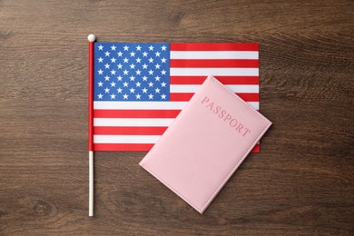 Photo of Passport in pink cover and flag of United States on wooden table, top view