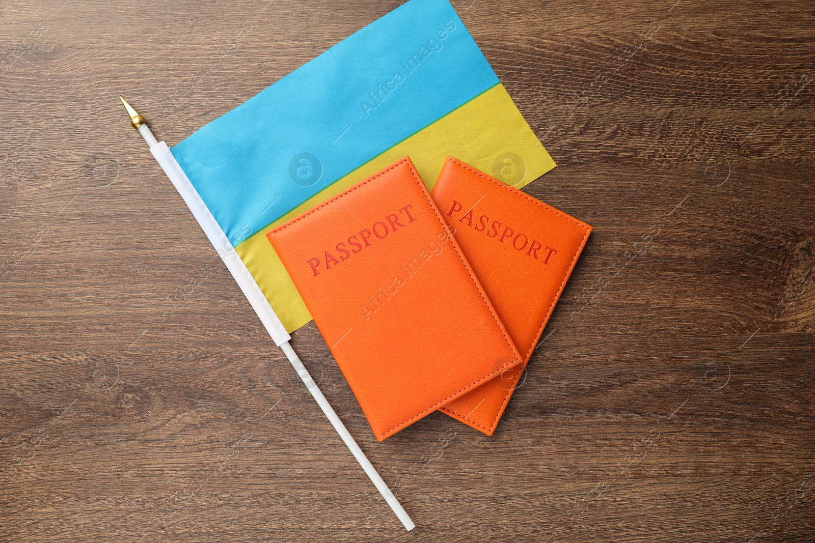 Photo of Passports in orange covers and flag of Ukraine on wooden table, top view