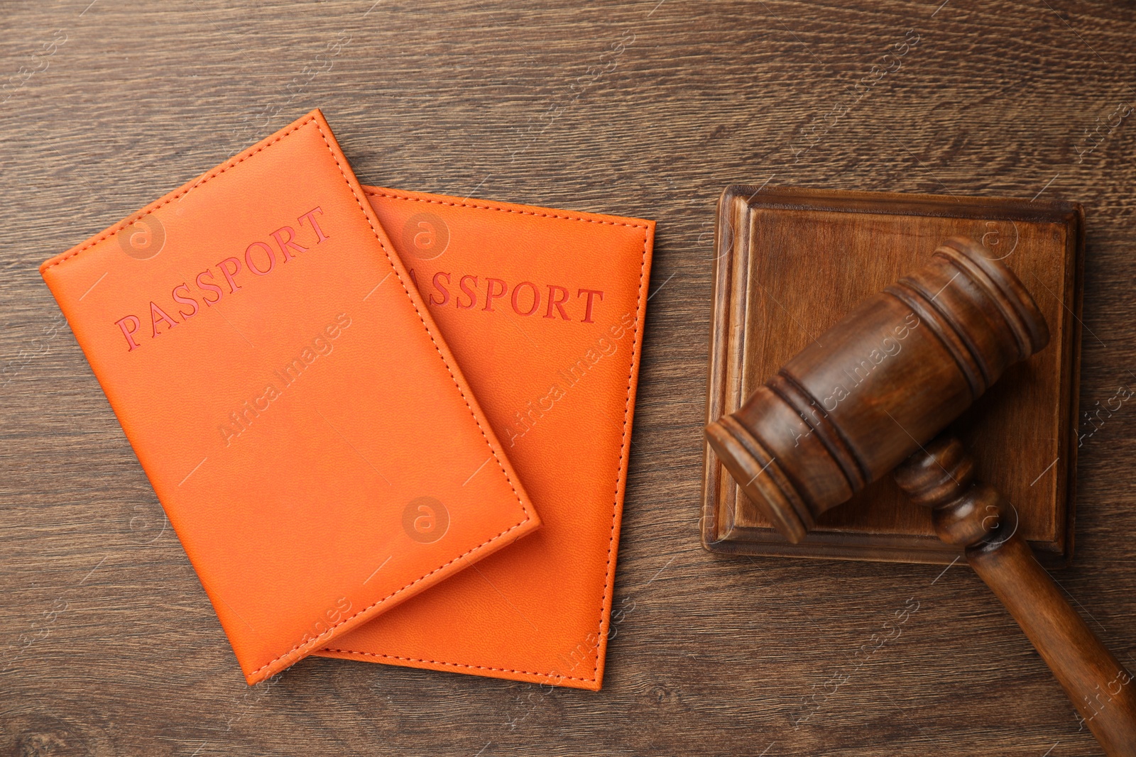 Photo of Passports in orange covers and judge's gavel on wooden table, top view