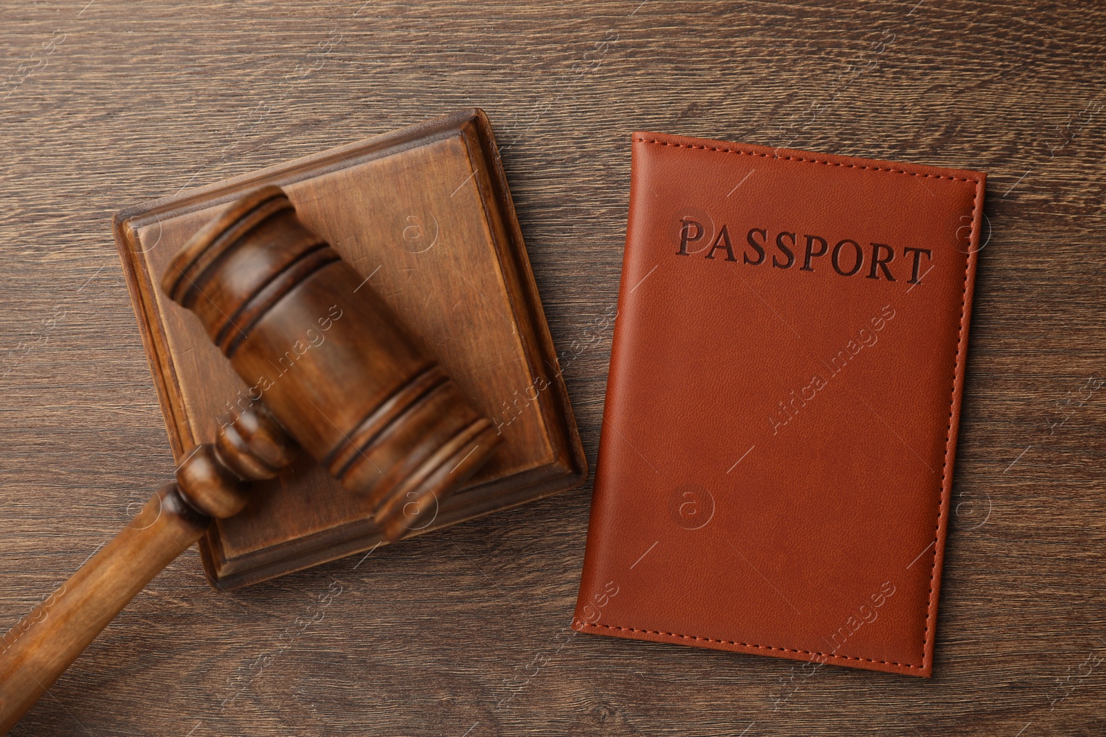 Photo of Passport in brown cover and judge's gavel on wooden table, top view