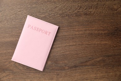 Photo of Passport in pink cover on wooden table, top view. Space for text