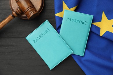 Photo of Passports in light blue covers, gavel and flag of European Union on black wooden table, top view