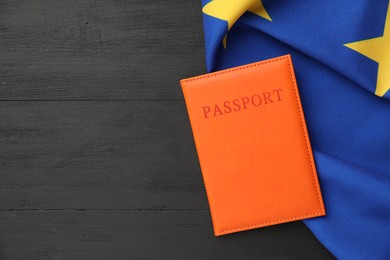 Passport in orange cover and flag of European Union on black wooden table, top view. Space for text