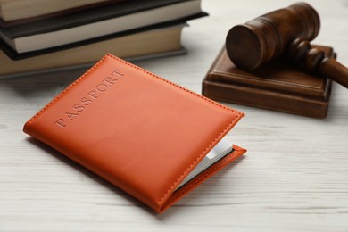 Photo of Passport in leather cover, judge's gavel and books on light wooden table, closeup