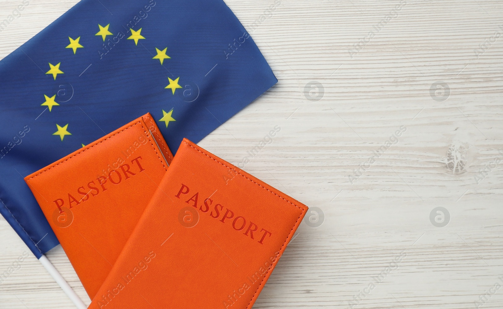 Photo of Passports in orange covers and flag of European Union on light wooden table, top view. Space for text