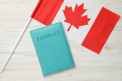 Photo of Passport in light blue cover and flag of Canada on wooden table, top view