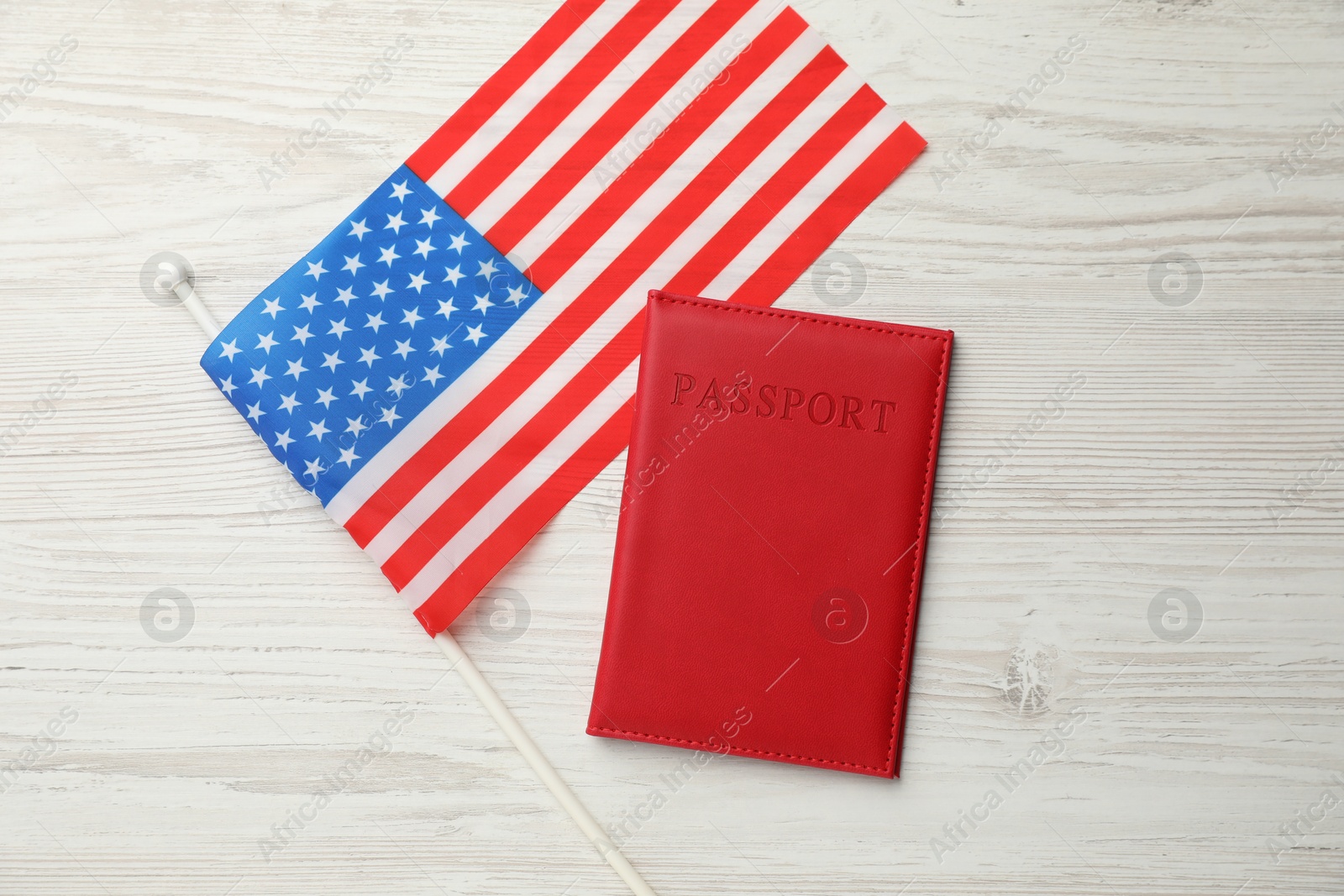 Photo of Passport in red cover and flag of United States on light wooden table, top view