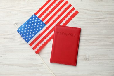 Photo of Passport in red cover and flag of United States on light wooden table, top view