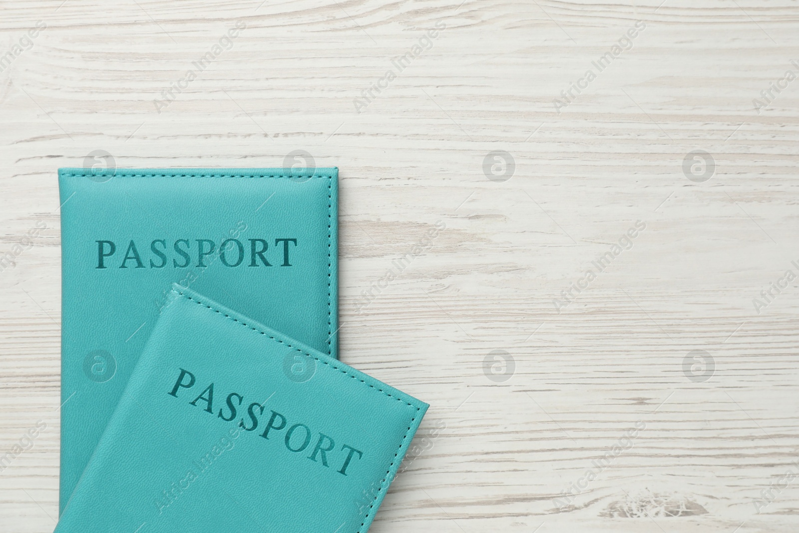 Photo of Passports in light blue covers on wooden table, top view. Space for text