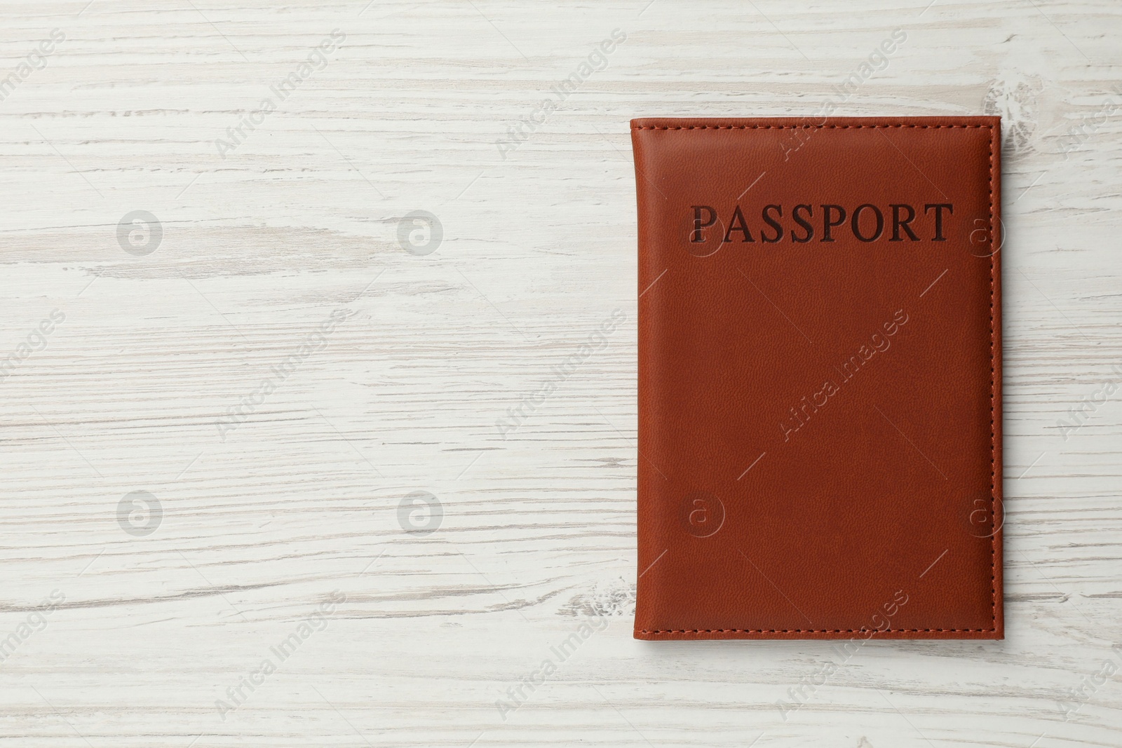 Photo of Passport in brown cover on light wooden table, top view. Space for text