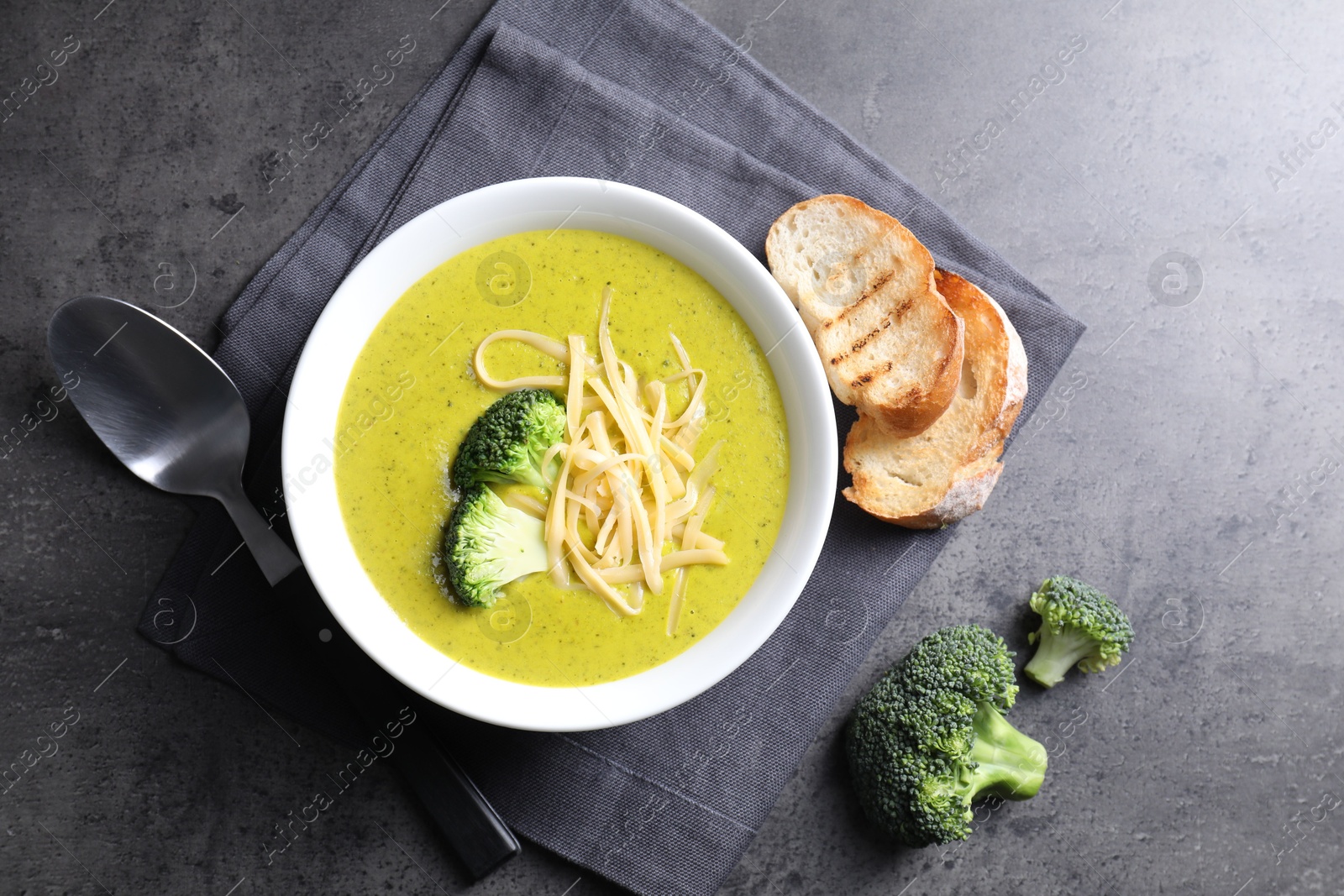 Photo of Delicious broccoli cream soup served on gray textured table, flat lay