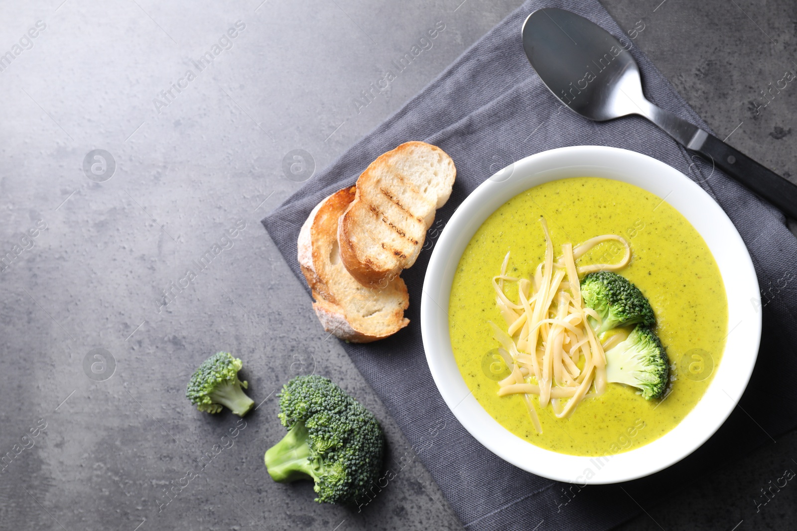 Photo of Delicious broccoli cream soup served on gray textured table, flat lay. Space for text