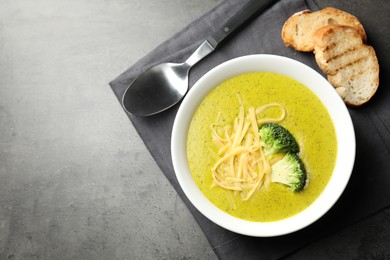 Photo of Delicious broccoli cream soup served on gray textured table, flat lay. Space for text