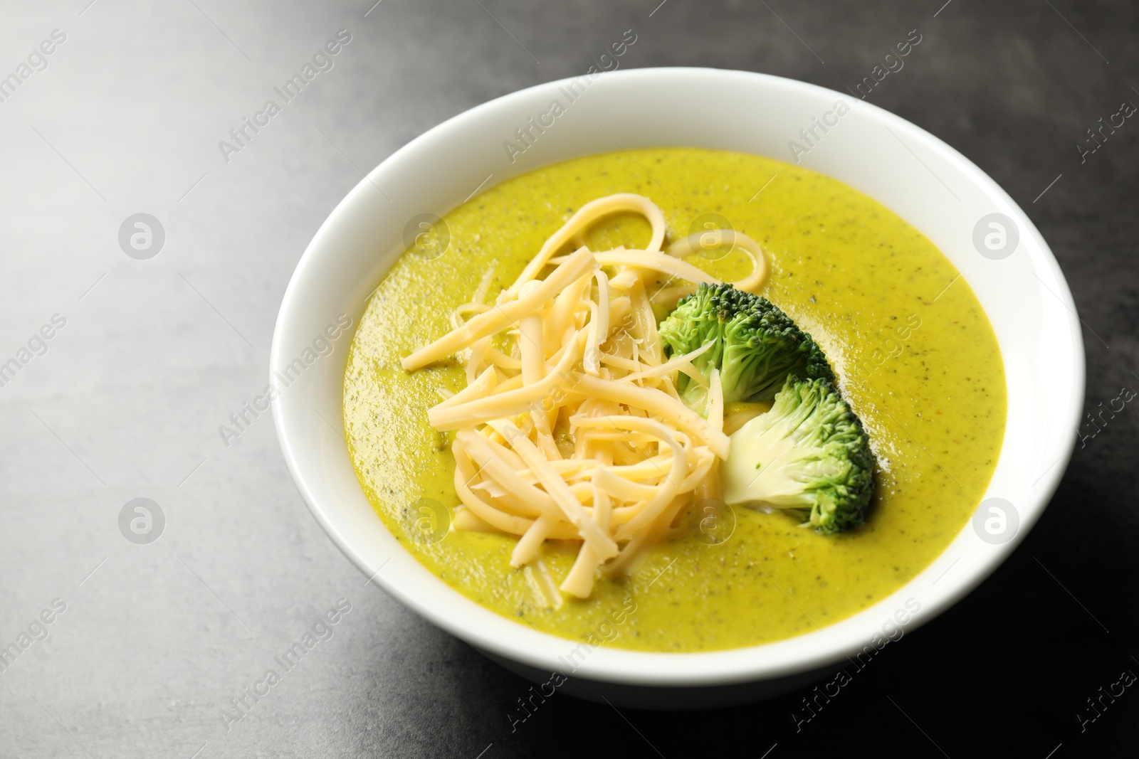 Photo of Delicious broccoli cream soup in bowl on gray textured table, closeup