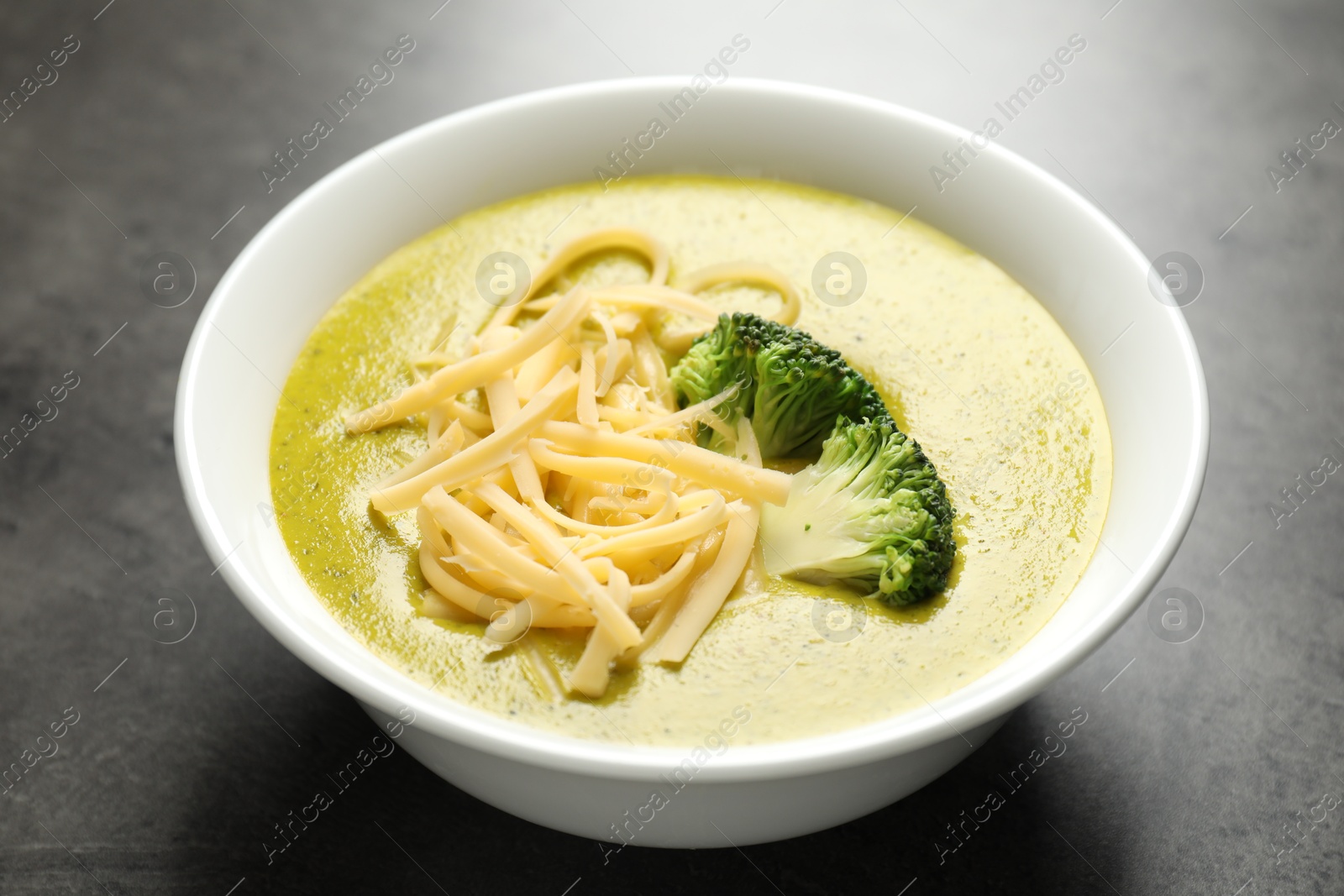 Photo of Delicious broccoli cream soup in bowl on gray textured table, closeup