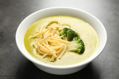 Photo of Delicious broccoli cream soup in bowl on gray textured table, closeup