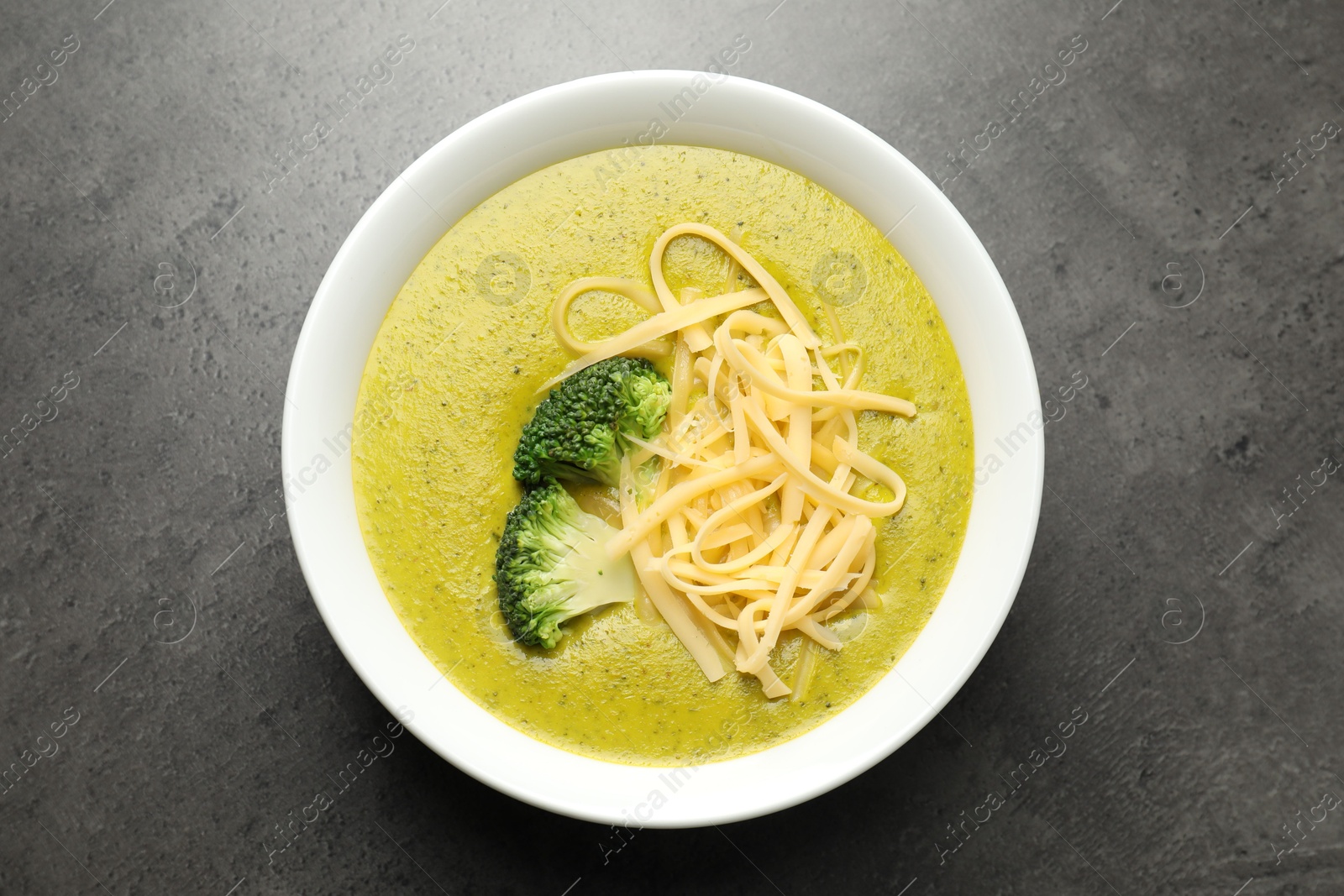 Photo of Delicious broccoli cream soup in bowl on gray textured table, top view