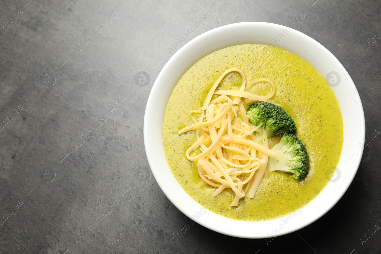 Photo of Delicious broccoli cream soup in bowl on gray textured table, top view. Space for text