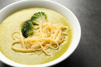 Photo of Delicious broccoli cream soup in bowl on gray textured table, closeup