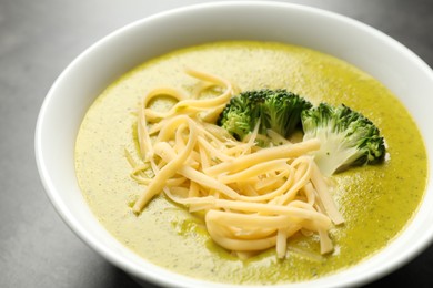 Photo of Delicious broccoli cream soup in bowl on gray table, closeup