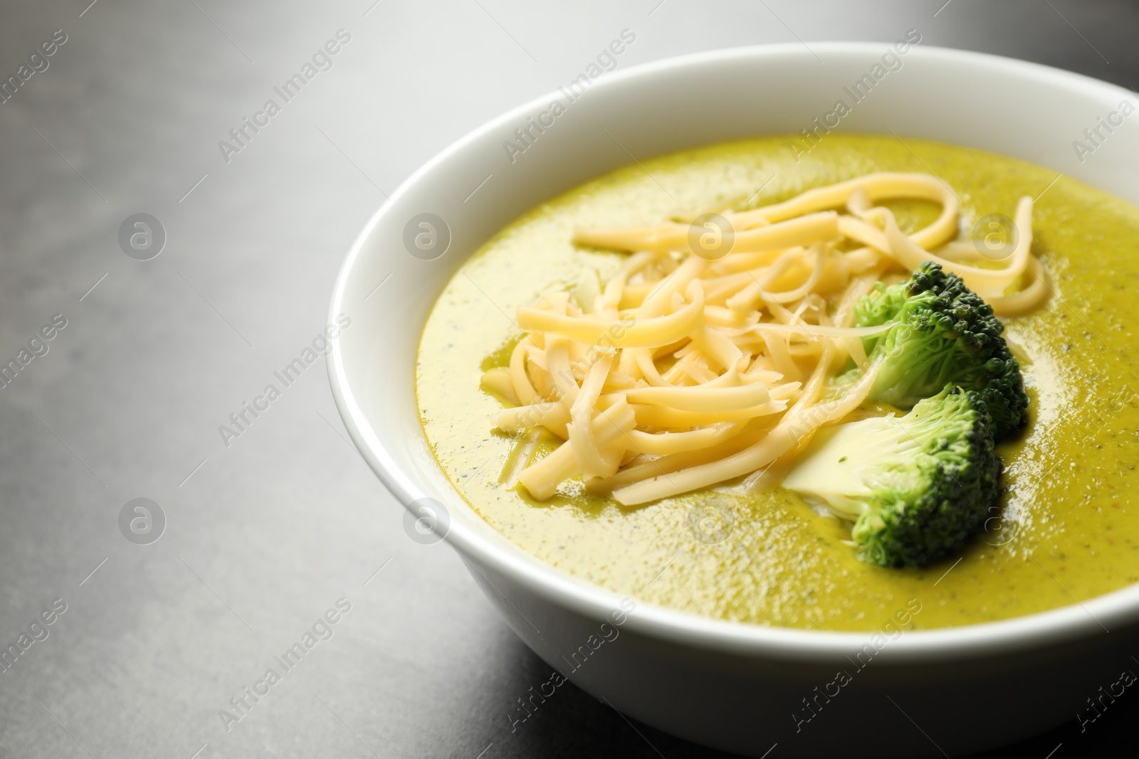 Photo of Delicious broccoli cream soup in bowl on gray table, closeup. Space for text