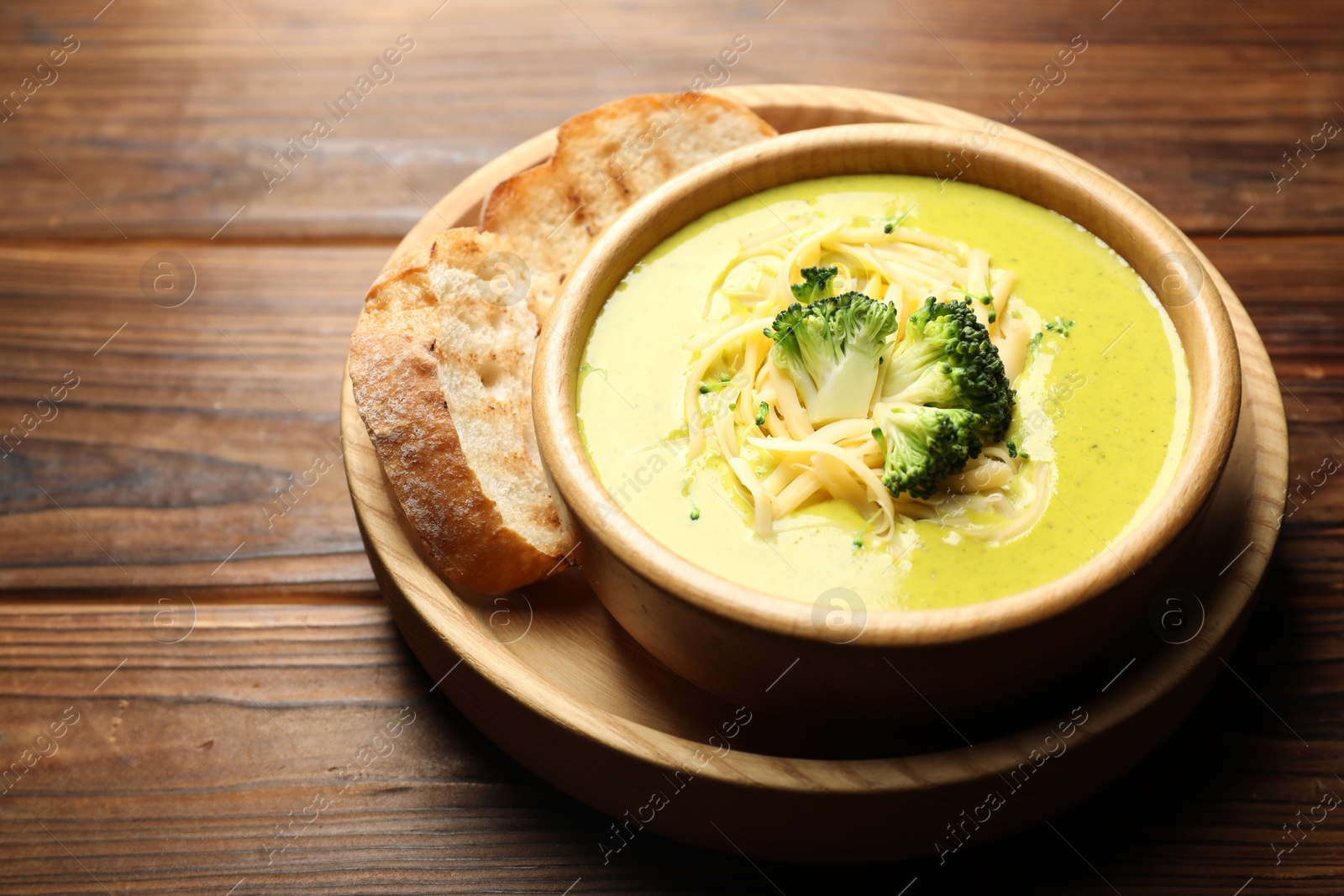 Photo of Delicious broccoli cream soup in bowl and croutons on wooden table, closeup