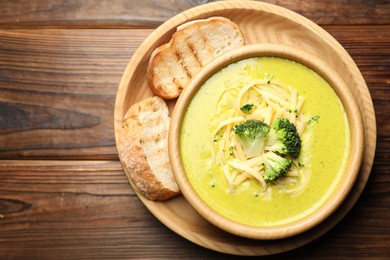 Photo of Delicious broccoli cream soup in bowl and croutons on wooden table, top view. Space for text