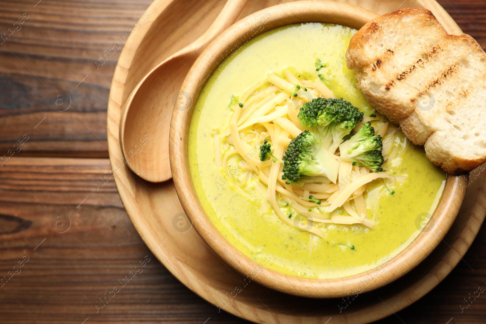 Photo of Delicious broccoli cream soup served on wooden table, top view