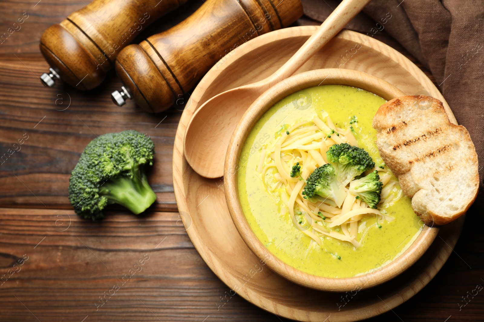 Photo of Delicious broccoli cream soup served on wooden table, flat lay