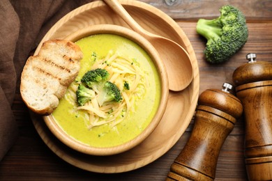 Photo of Delicious broccoli cream soup served on wooden table, flat lay