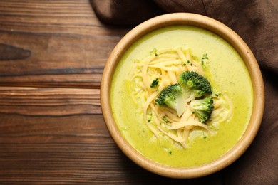 Photo of Delicious broccoli cream soup in bowl on wooden table, top view. Space for text