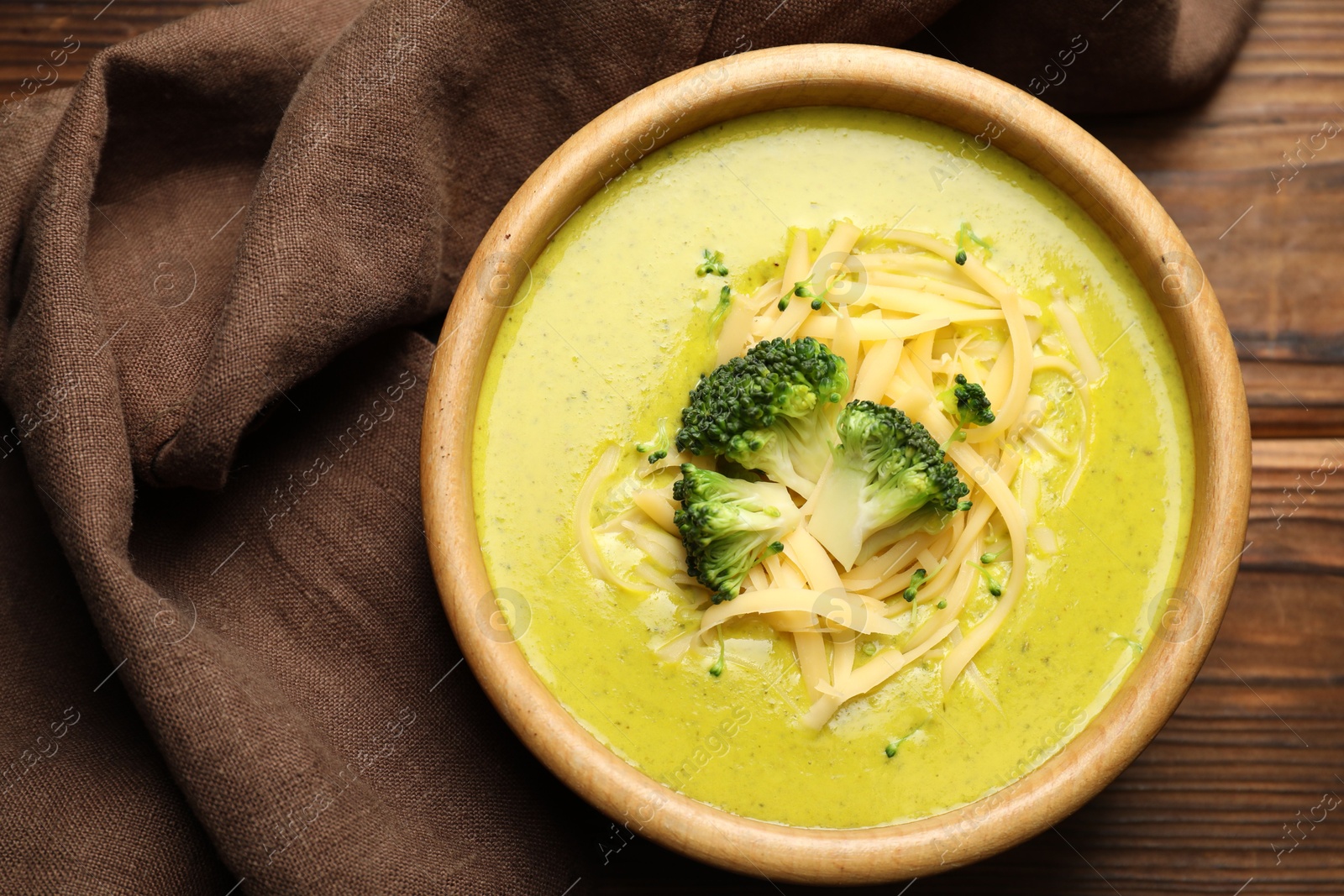 Photo of Delicious broccoli cream soup in bowl on wooden table, top view