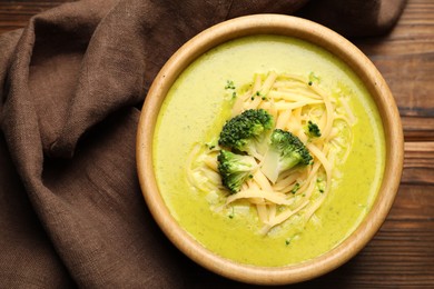 Photo of Delicious broccoli cream soup in bowl on wooden table, top view