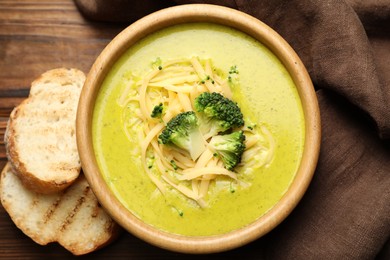 Photo of Delicious broccoli cream soup in bowl and croutons on wooden table, flat lay