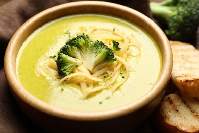 Photo of Delicious broccoli cream soup in bowl and croutons on table, closeup