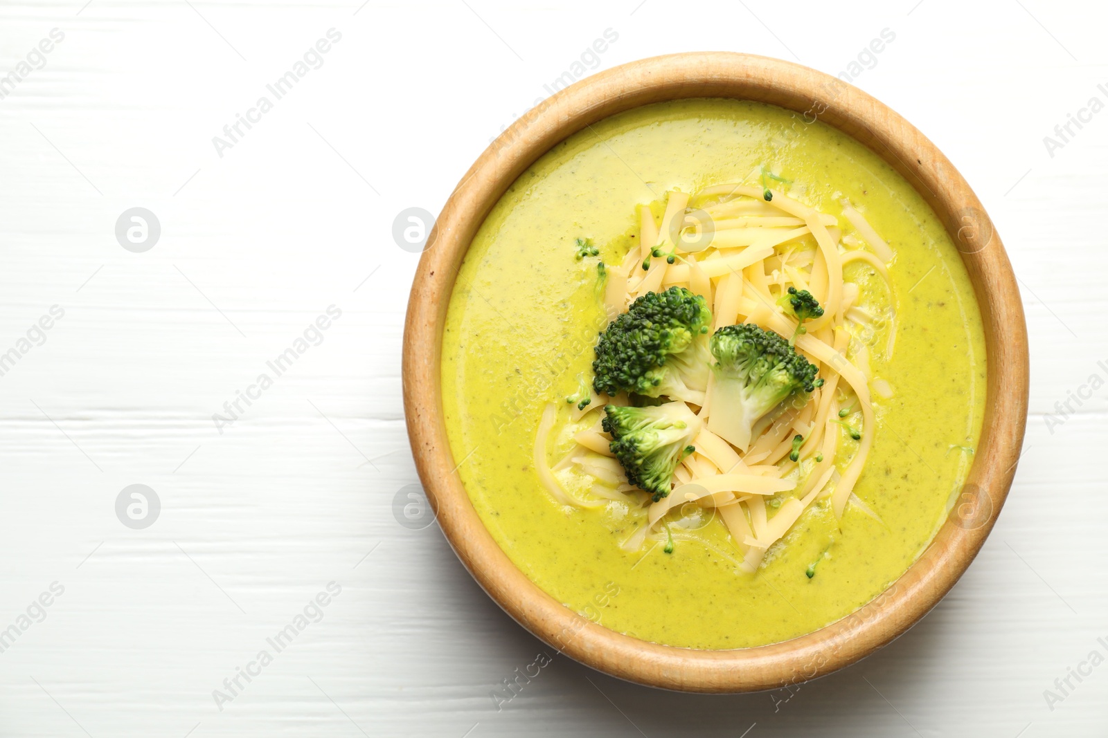 Photo of Delicious broccoli cream soup in bowl on white wooden table, top view. Space for text