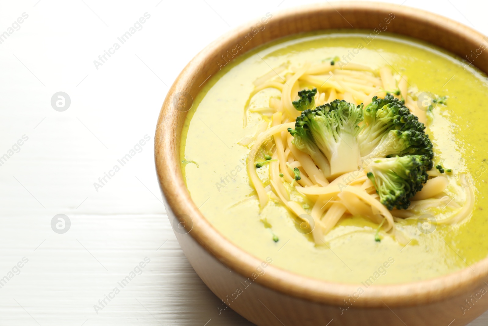 Photo of Delicious broccoli cream soup in bowl on white wooden table, closeup. Space for text