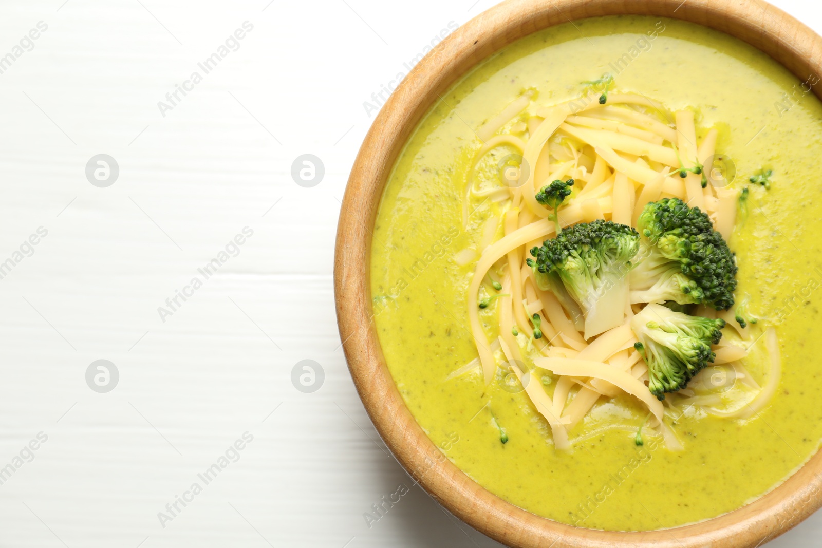 Photo of Delicious broccoli cream soup in bowl on white wooden table, top view. Space for text