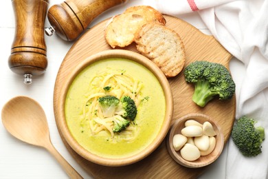 Photo of Delicious broccoli cream soup served on white wooden table, flat lay