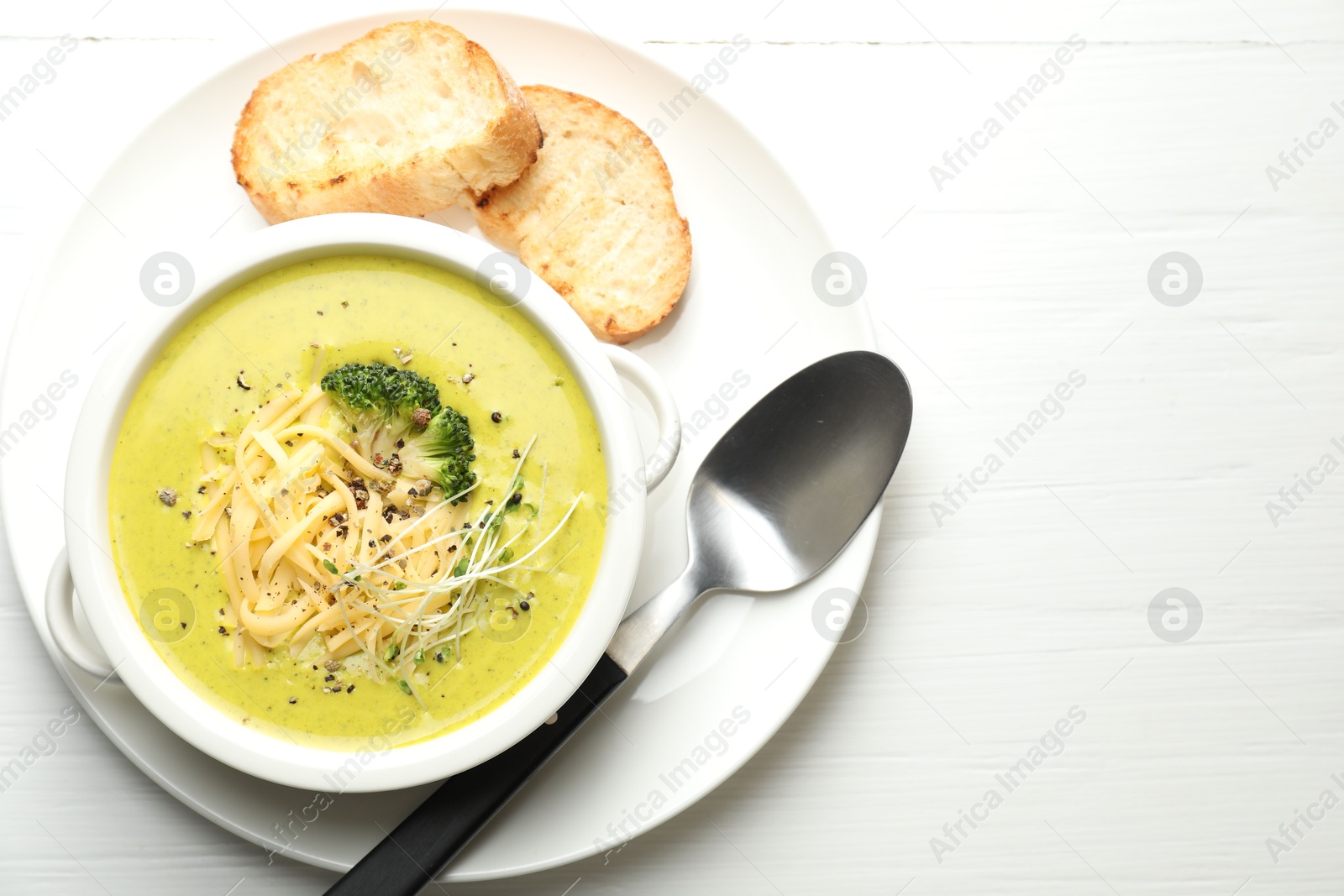 Photo of Delicious broccoli cream soup served on white wooden table, flat lay. Space for text