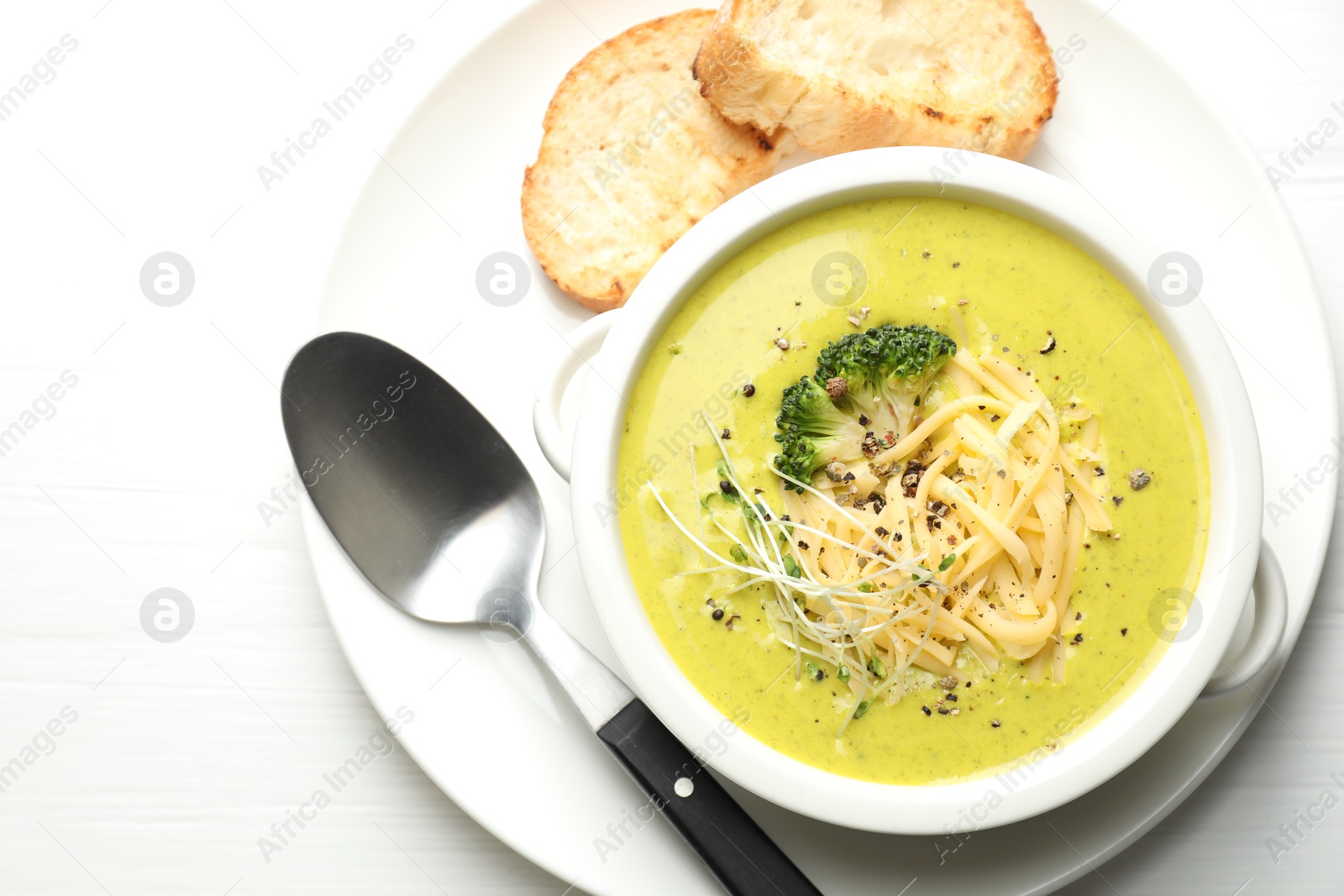 Photo of Delicious broccoli cream soup served on white wooden table, flat lay