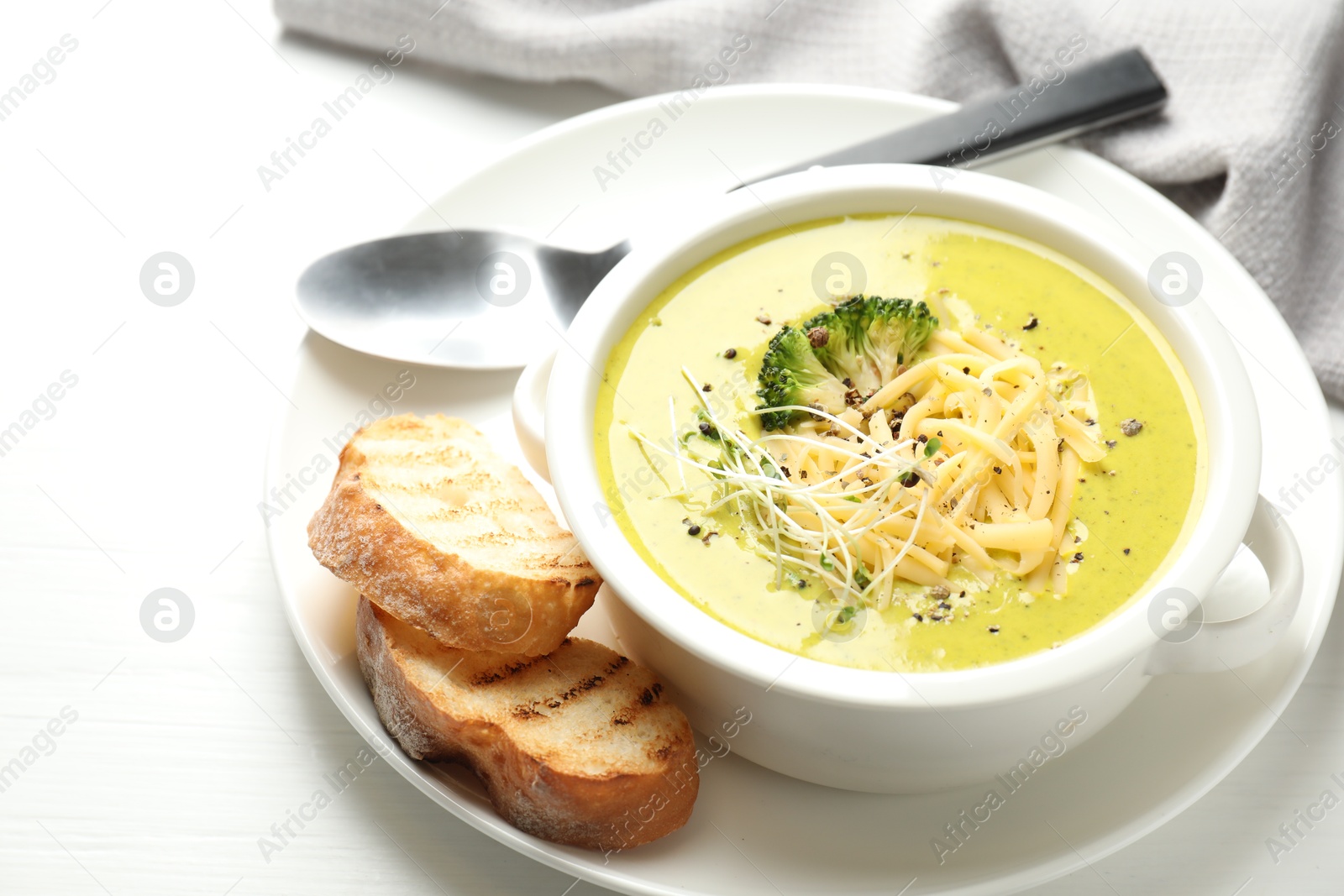 Photo of Delicious broccoli cream soup served on white wooden table, closeup