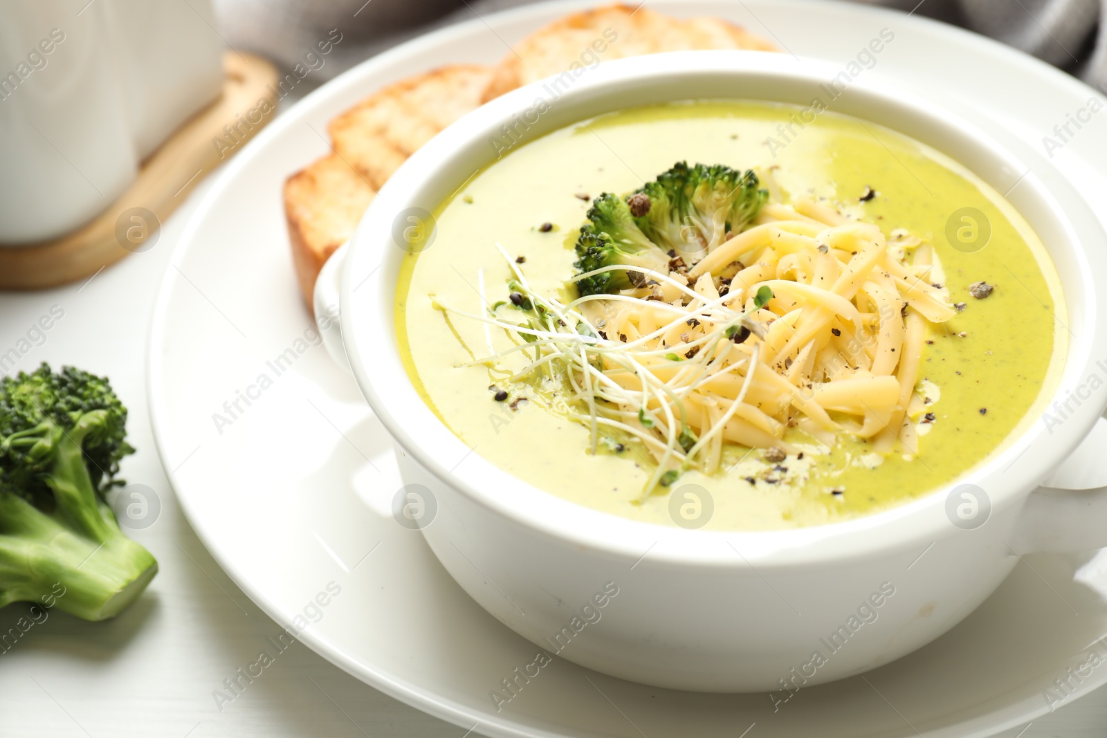 Photo of Delicious broccoli cream soup served on white wooden table, closeup