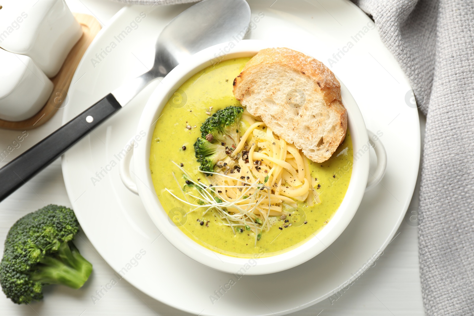 Photo of Delicious broccoli cream soup served on white wooden table, flat lay