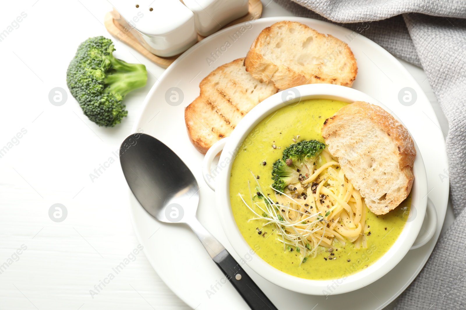 Photo of Delicious broccoli cream soup served on white wooden table, flat lay