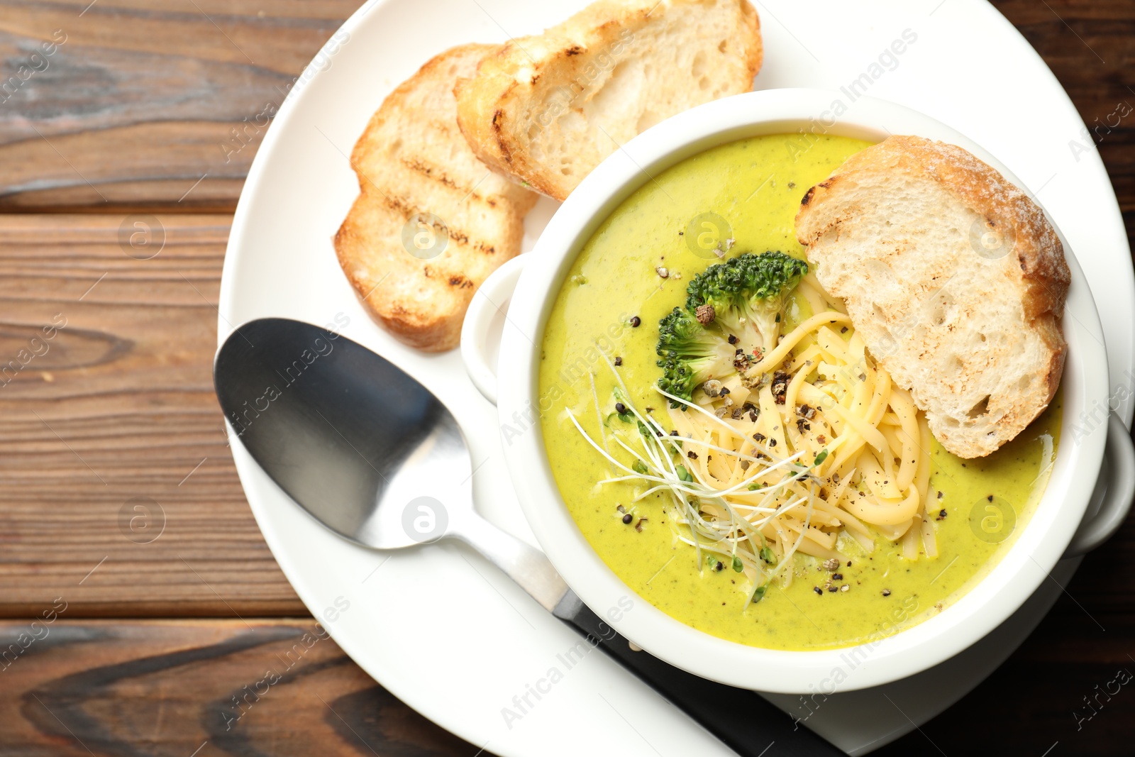 Photo of Delicious broccoli cream soup served on wooden table, top view