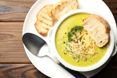 Photo of Delicious broccoli cream soup served on wooden table, top view